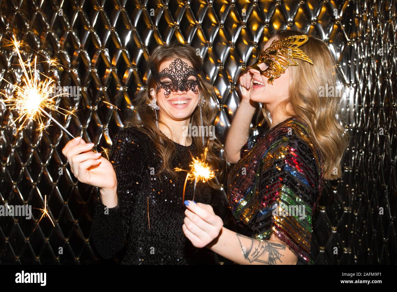 Joyful girls in venetian masks holding sparkling bengal lights while having fun Stock Photo