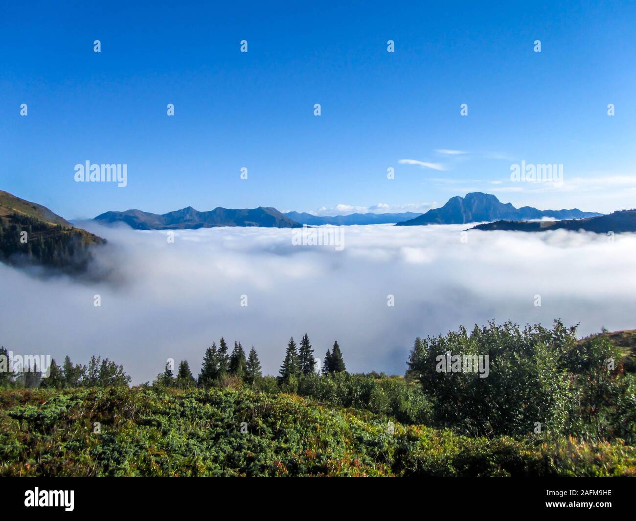 A panoramic view on Alpine valley. The valley is shrouded in dense fog, only tall mountain peaks are visible. Hiking trails in the high mountain. Endl Stock Photo