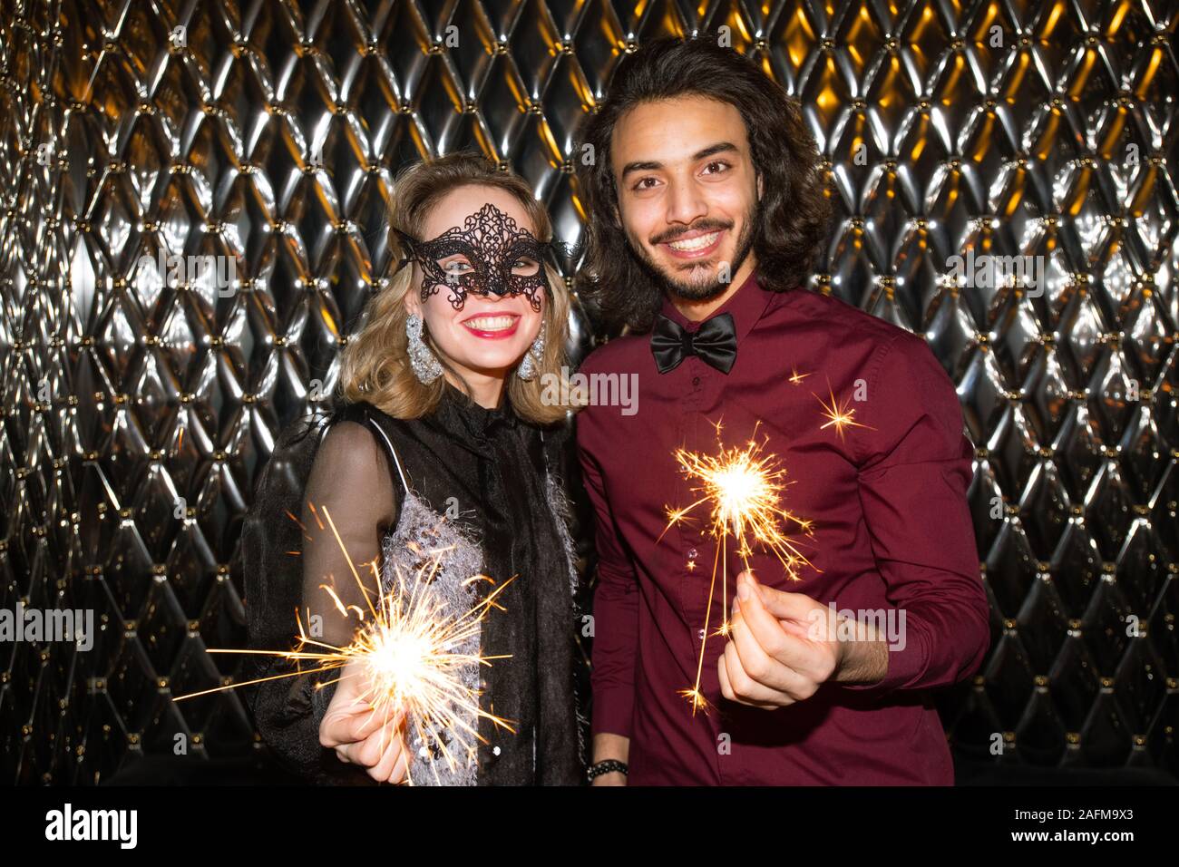 Happy girl in venetian mask and guy with sparkling bengal lights looking at you Stock Photo