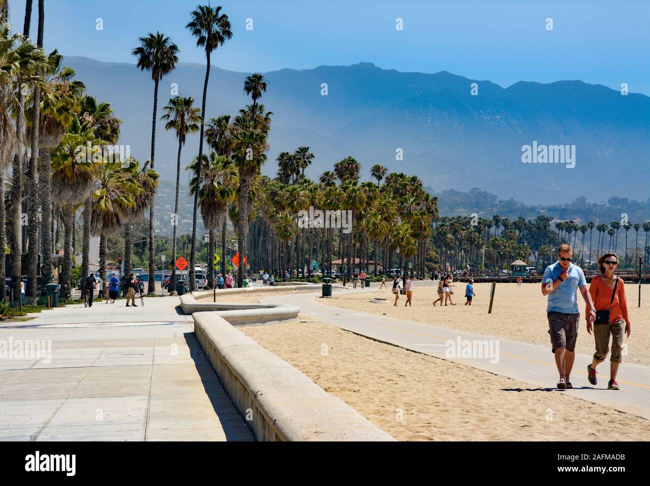 A couple walks along a pathway on the beach  along side palm tree lined Cabrillio Boulevard in Santa Barbara, CA, Stock Photo