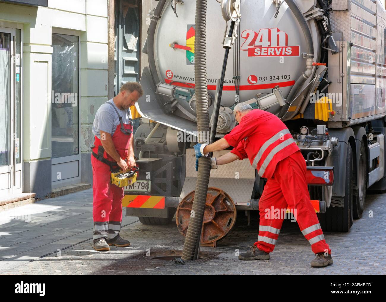 CELJE, Slovenia - August 1, 2019: Two workmen inserting a hose in a manhole for sewage system maintenance in a downtown street Stock Photo