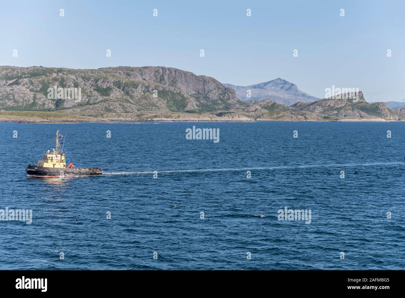 near VAGOYA, NORWAY - July 17 2019: fjord landscape with tugboat towing in fjord waters, shot under bright summer light on july 17, 2019 near Vagoya i Stock Photo