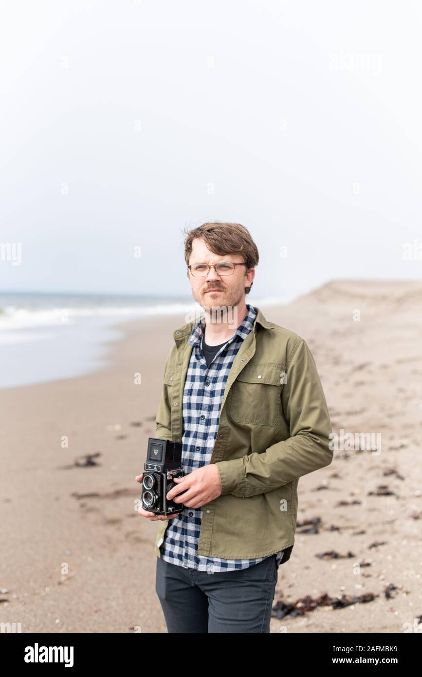 Portrait of young man holding film camera on beach Stock Photo