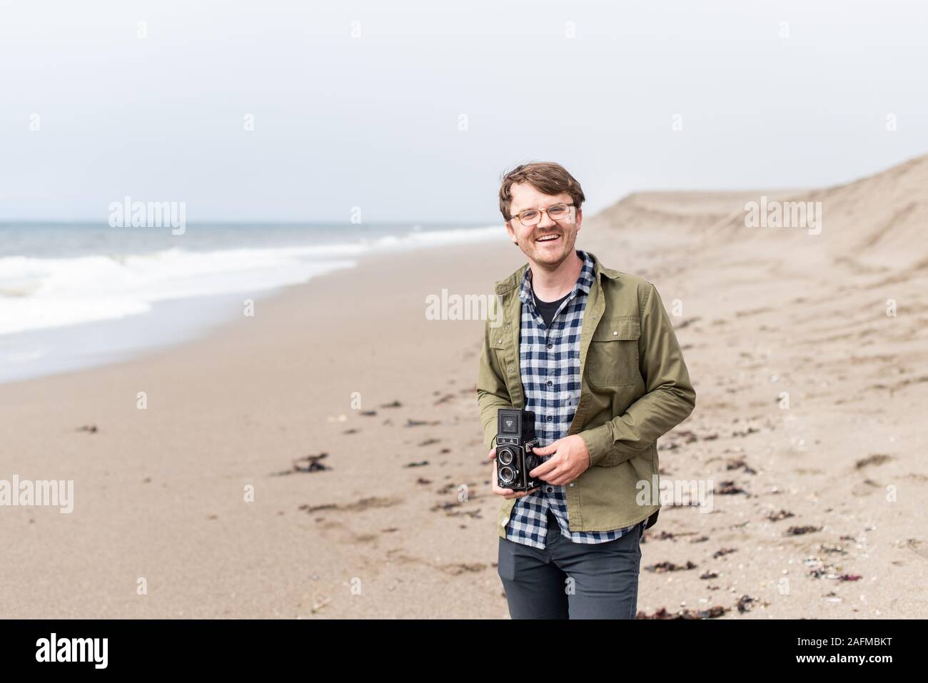 Portrait of young man laughing while holding film camera on beach Stock Photo