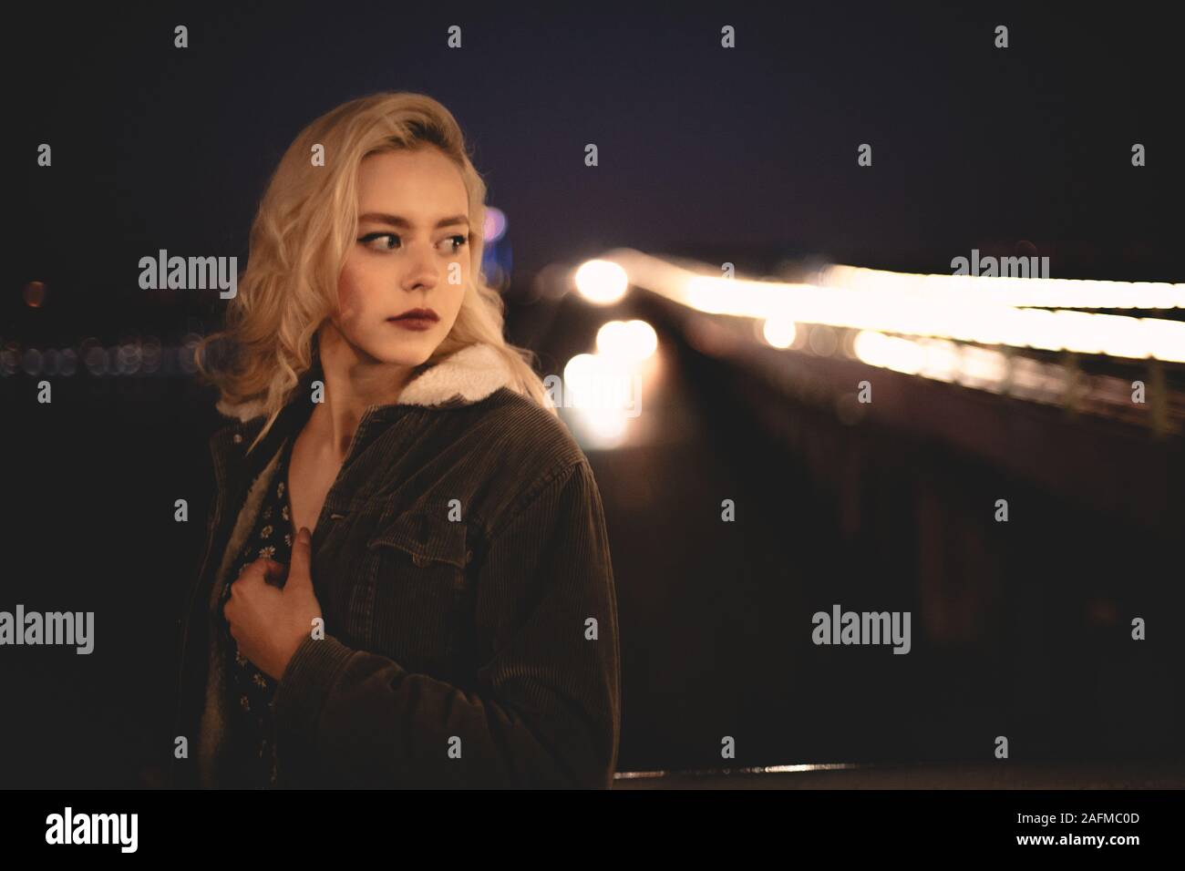 Portrait of young woman standing against illuminated bridge in city Stock Photo