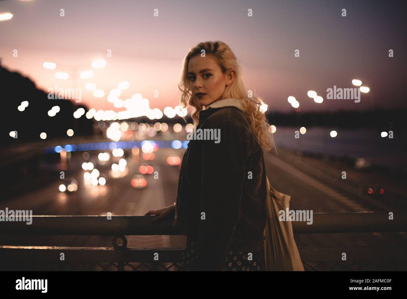 Young woman standing on bridge in city against sky at sunset Stock Photo