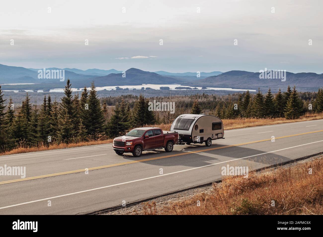 Pickup truck and RV camper drive along scenic road in Jackman, Maine