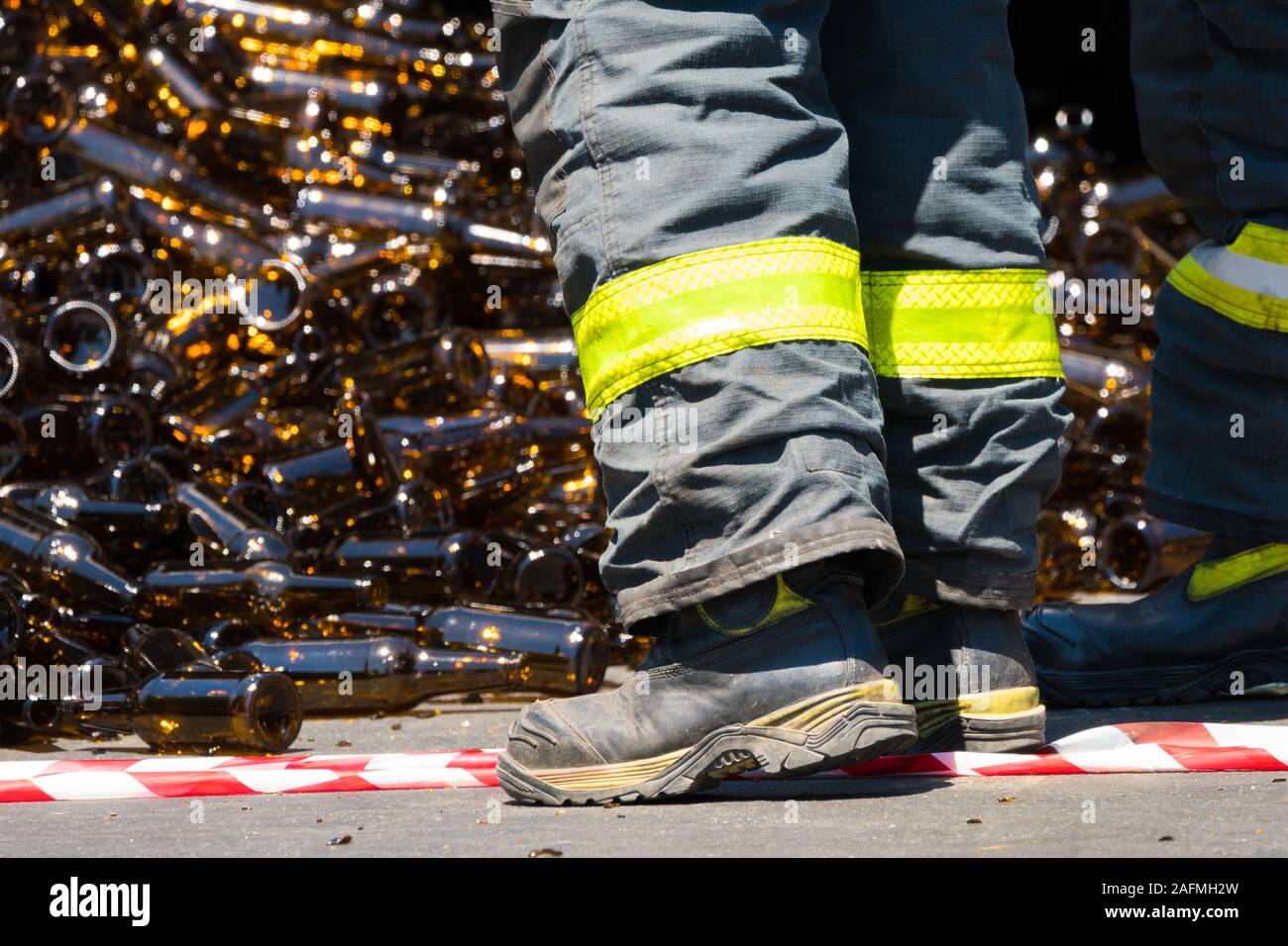 fireman, firefighter, emergency worker wearing high visibility pants and boots in the road with a heap of glass bottles at an accident scene cleanup Stock Photo