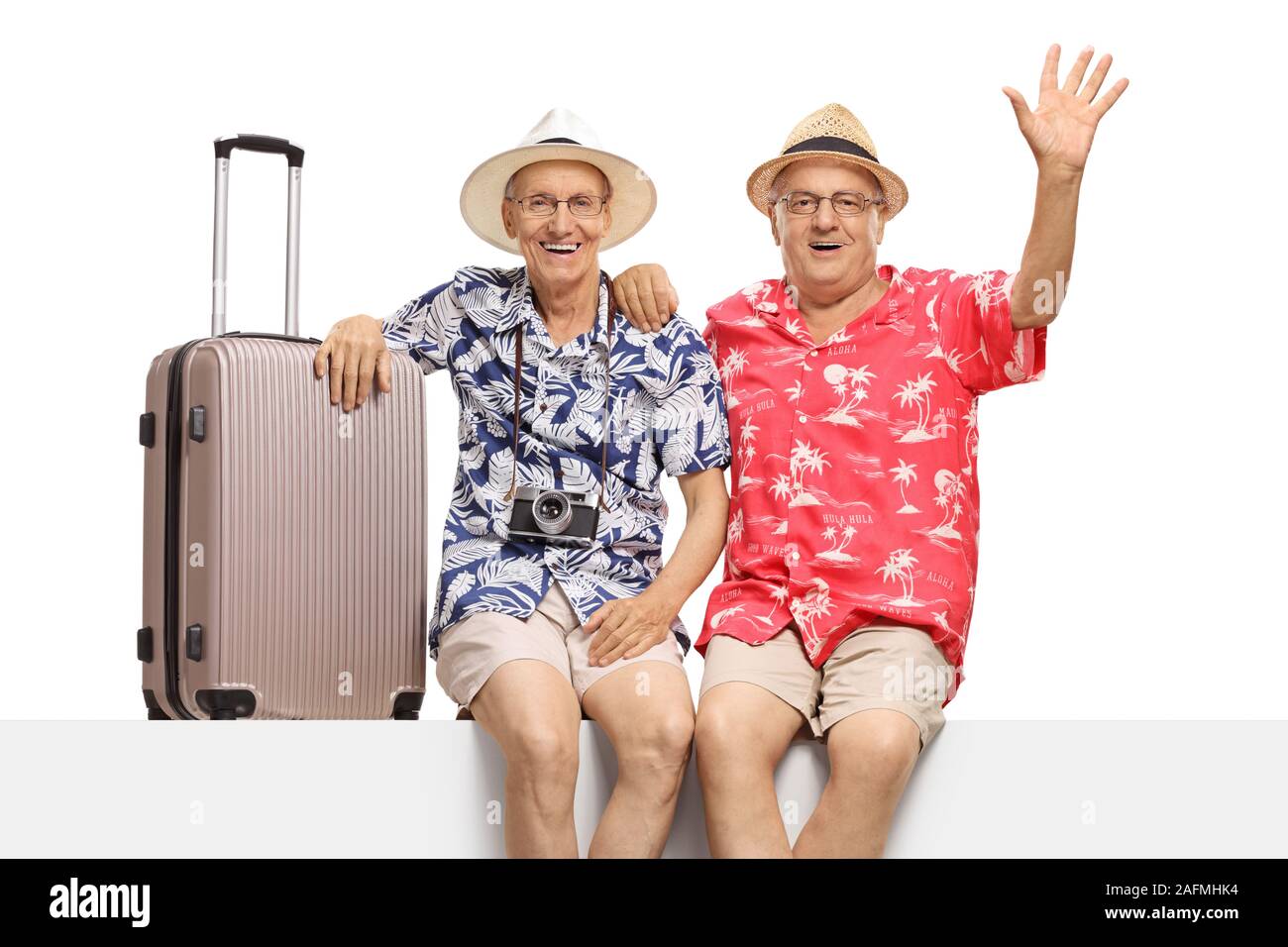 Senior male tourists sitting on a panel with a suitcase and waving at the camera isolated on white background Stock Photo