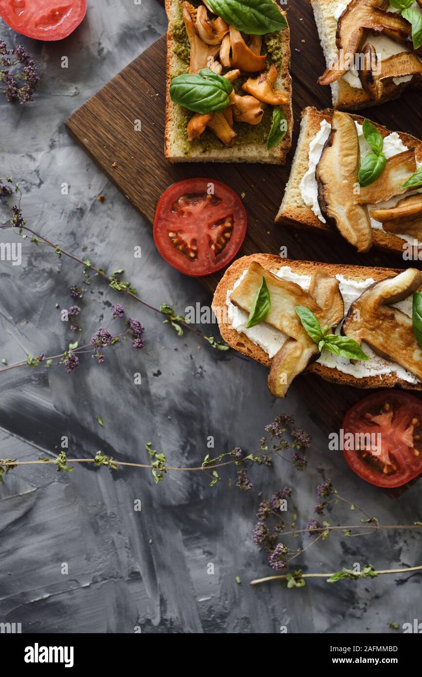 Healthy vegetarian snack. Bruschettas with chanterelle and porcini mushrooms with tomato and basil leaves on dark background top view copy space Stock Photo