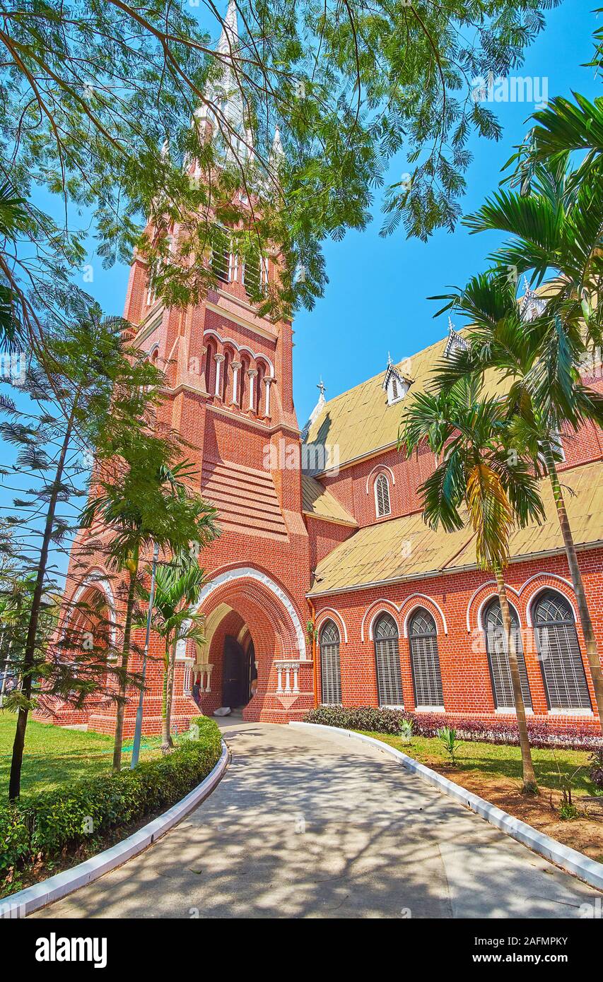 The shady garden alley leads to the tall belfry of Holy Trinity Anglican Church, Yangon, Myanmar Stock Photo