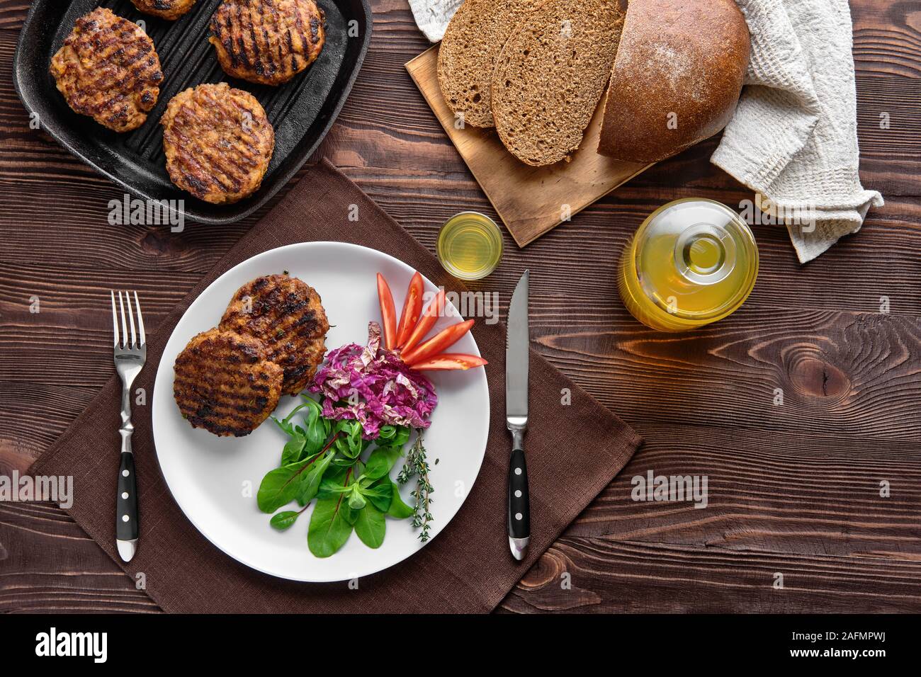 Top view of country dinner with cutlet and fresh salad, brown bread and moonshine on rustic wooden table Stock Photo