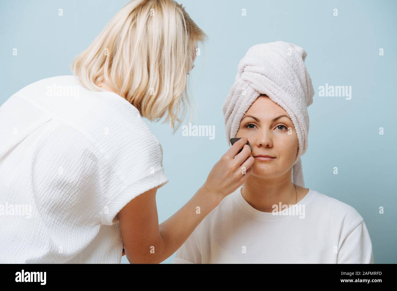 Female hairdresser applying setting powder on client's cheeks over blue. Stock Photo