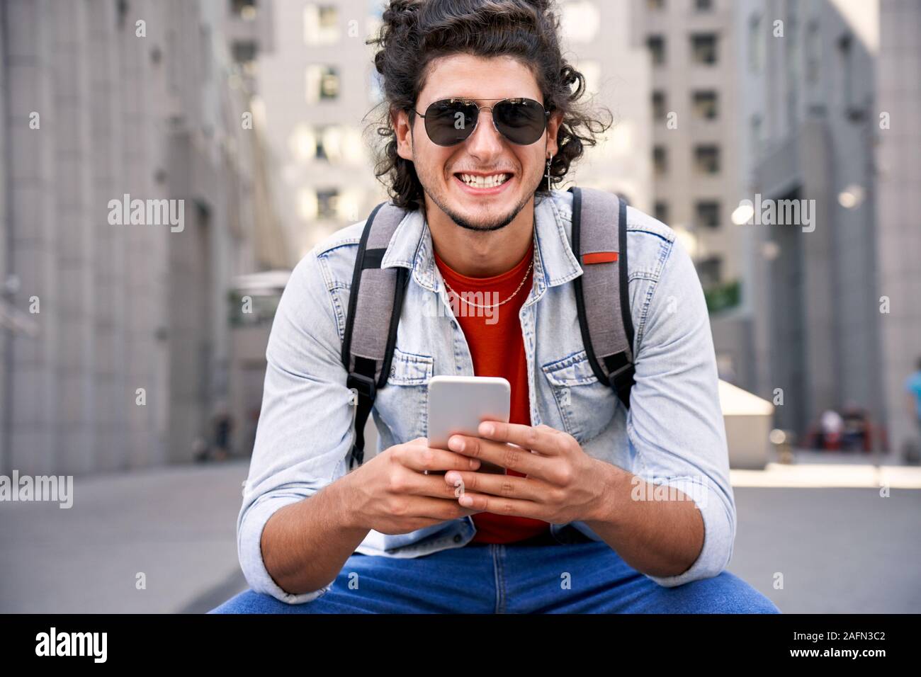Young adult man smiling and using smartphone Stock Photo