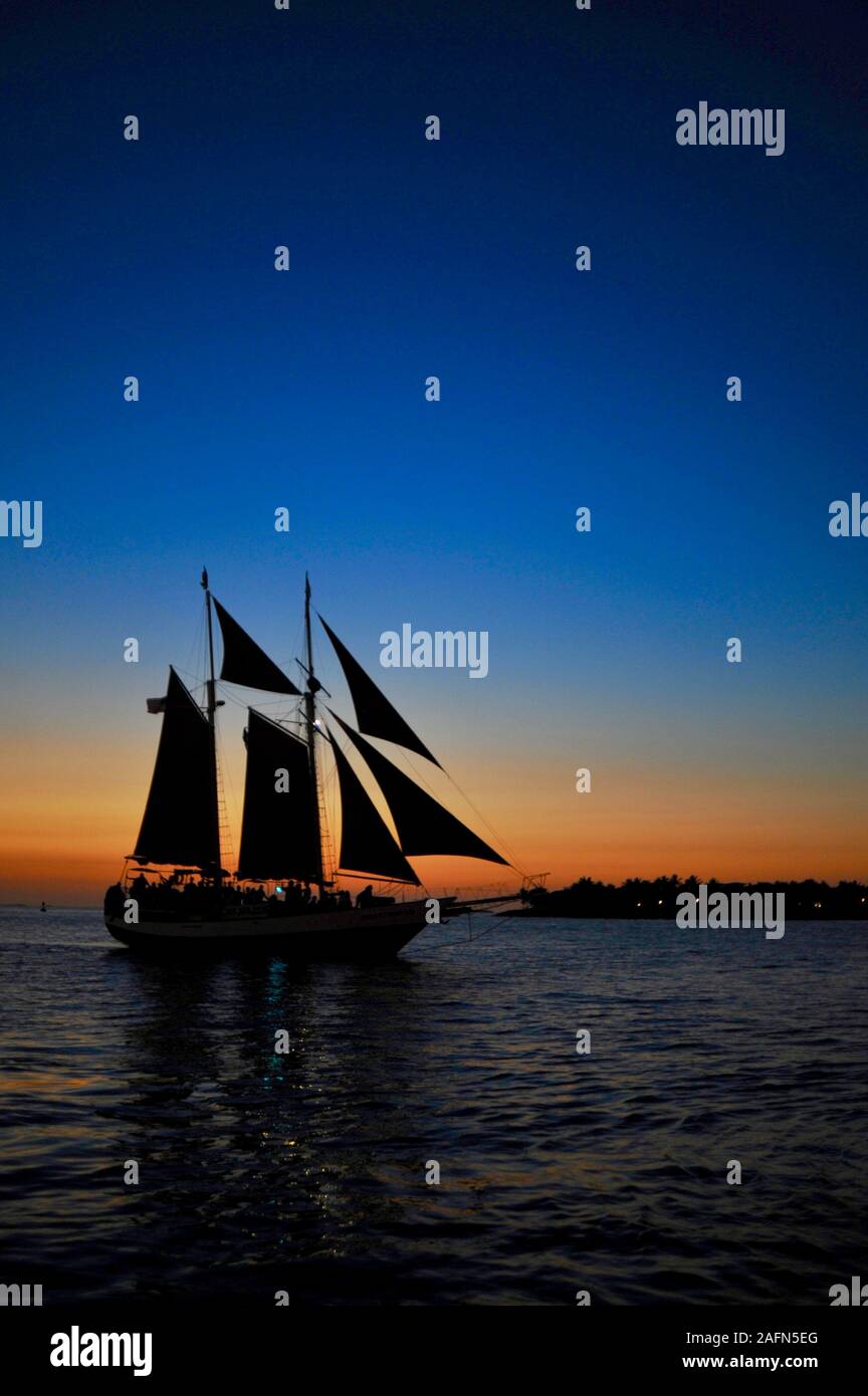 Sailboat out on calm waters for sunset cruise off Mallory Square in popular and famous tourist vacation spot in tropical Key West, Florida, USA Stock Photo