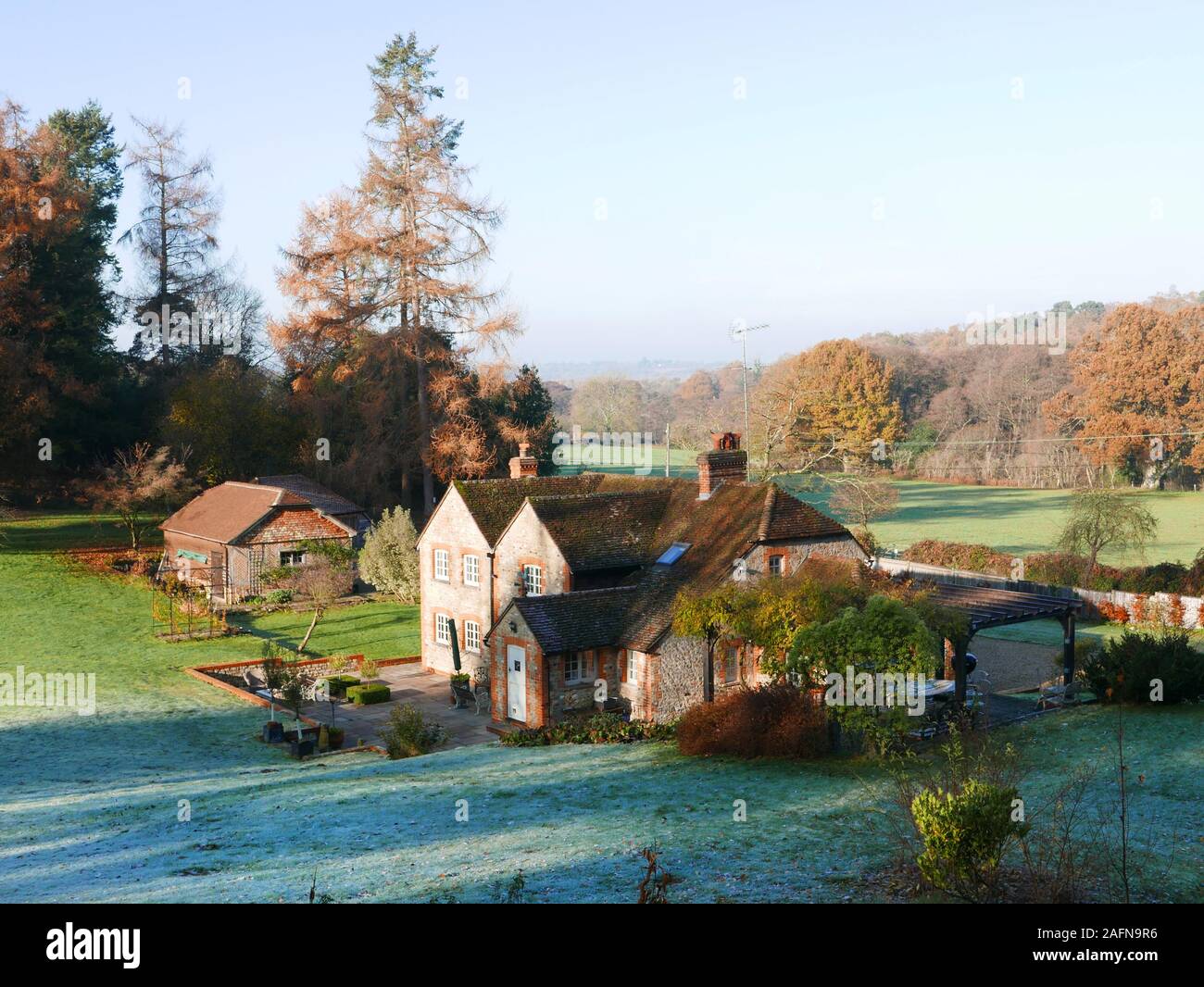Quintessential English Country cottage in misty valley surrounded by trees with frost and dew on a green grass lawn Stock Photo