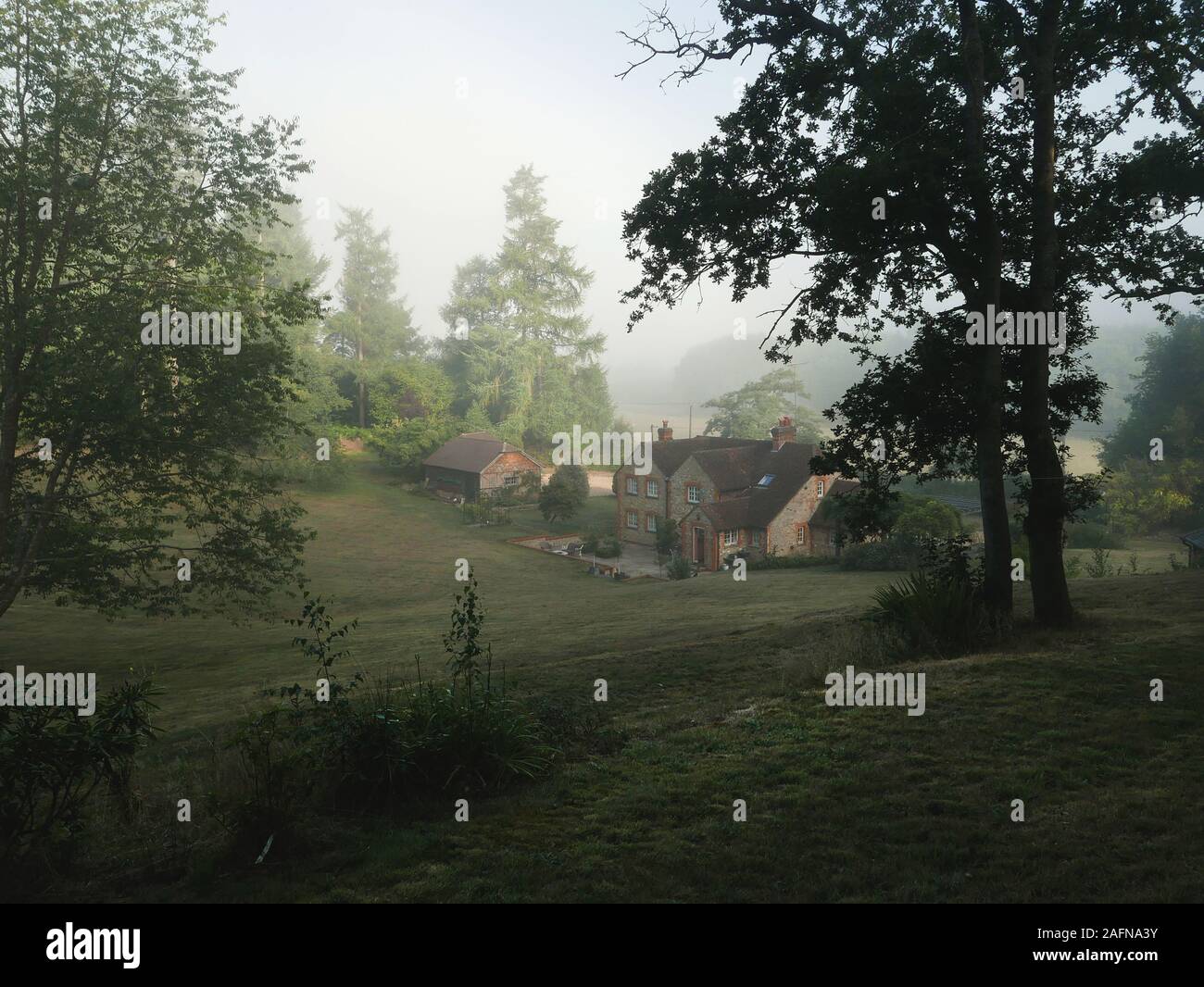 Quintessential English Country cottage in misty valley surrounded by trees Stock Photo