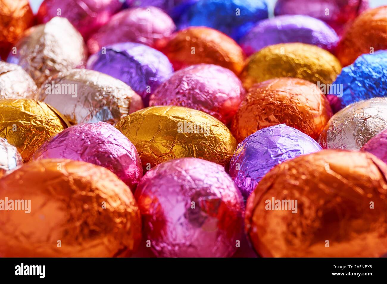 Many chocolate easter eggs wrapped in blue, purple, orange, pink and golden foil wrap Stock Photo