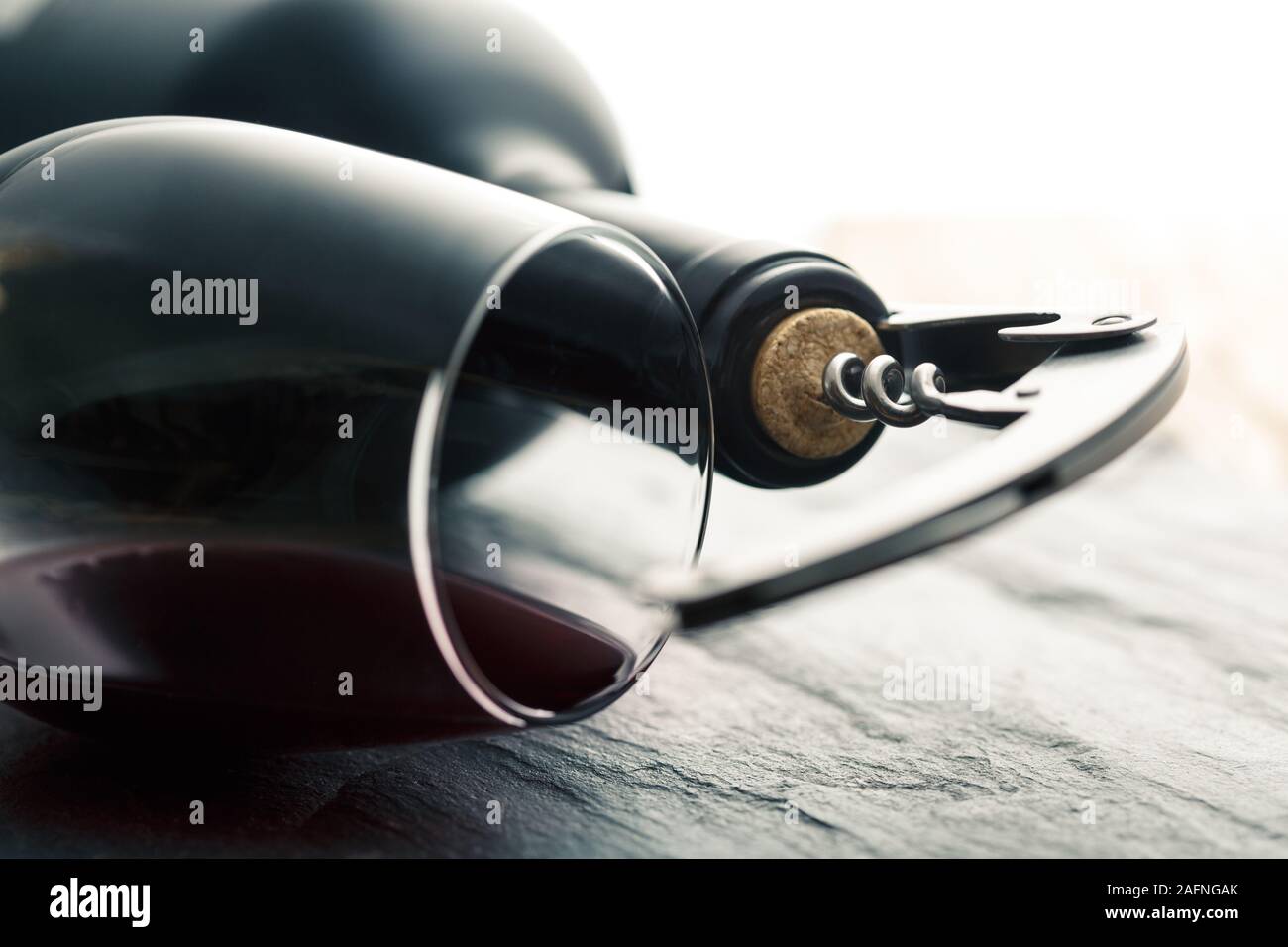 Stainless wine corkscrew in a cork of wine bottle neck and wine glass with wine lying on a black rocky slate background Stock Photo