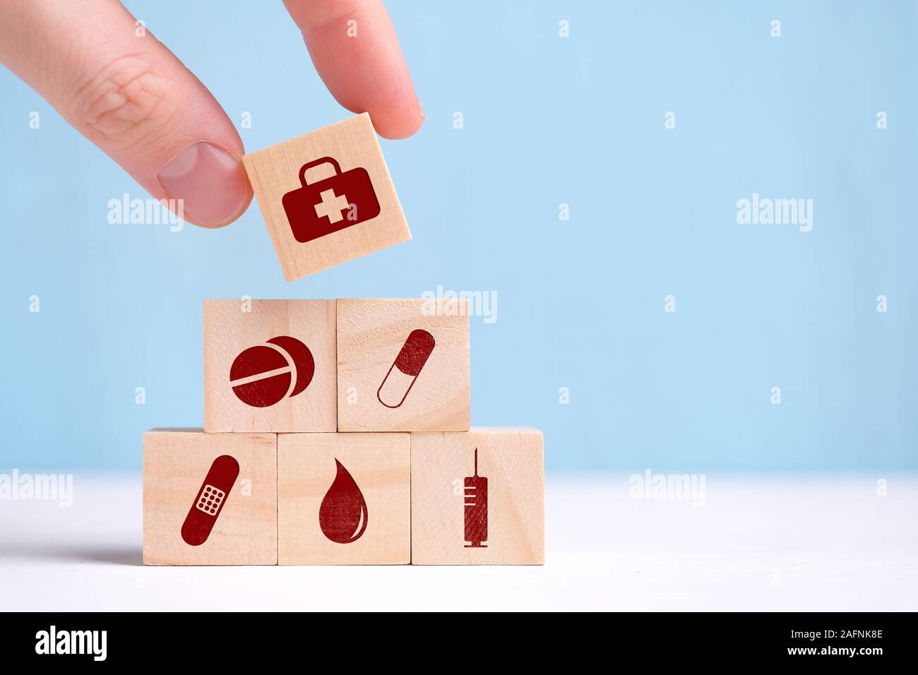 The hand holds a wooden cube with icons - tablets, capsule, Band-Aid, tests, syringe. Close up. Stock Photo