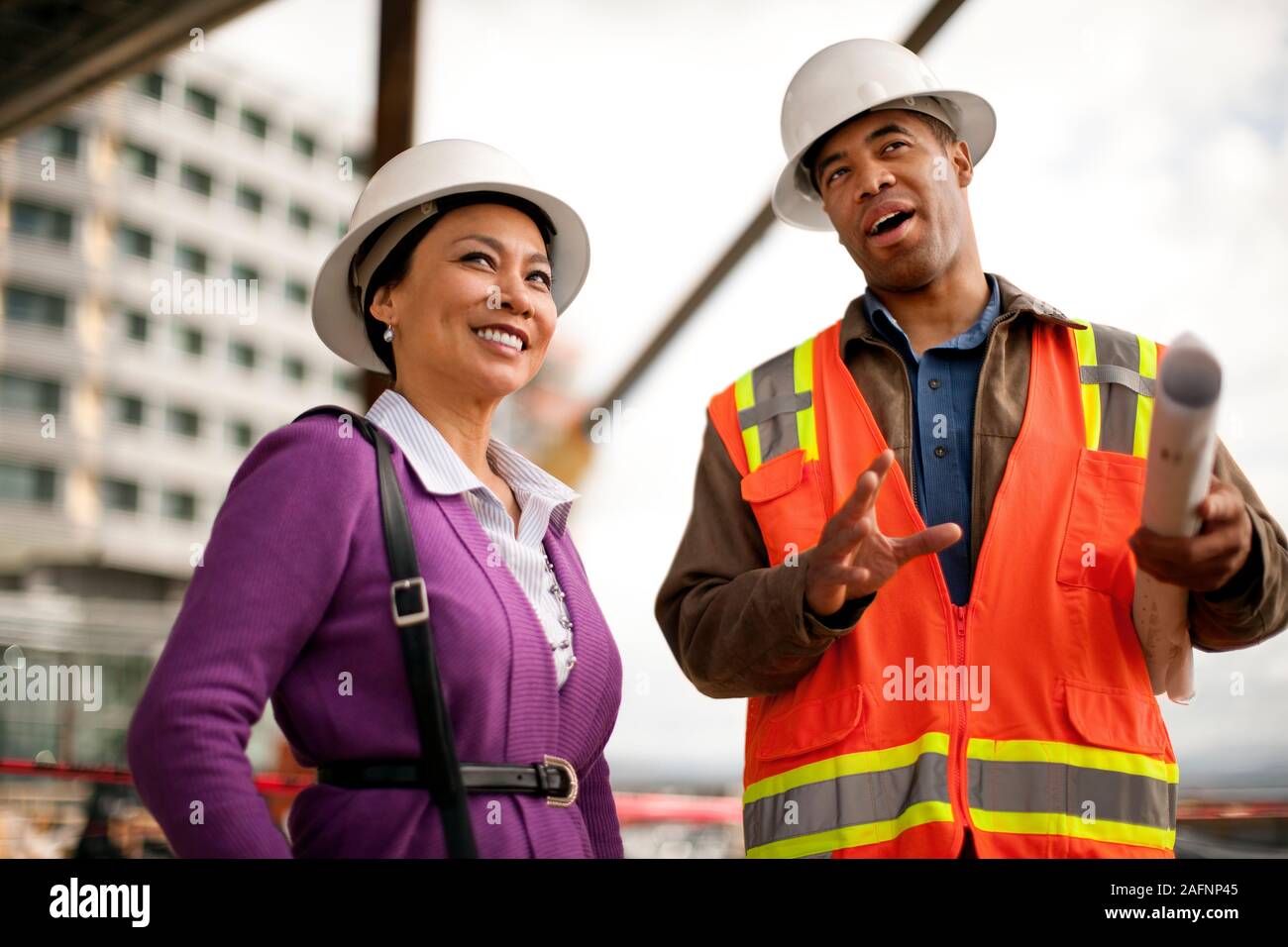 Two smiling engineers discussing plans on a construction site. Stock Photo