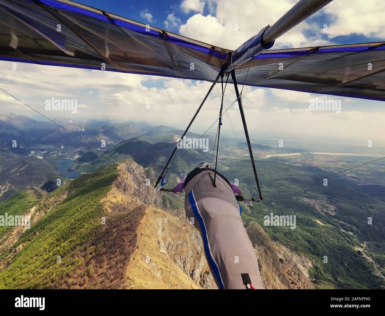 Hang gliding in the mountains. Hang glider pilot fly high above beautiful terrain in Meduno, Italy. Stock Photo