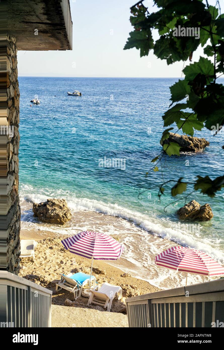 Small secluded beach with umbrellas and sunbeds on a sunny summer day, turquoise transparent water, view from above. Ionian sea coast, Albania. Stock Photo