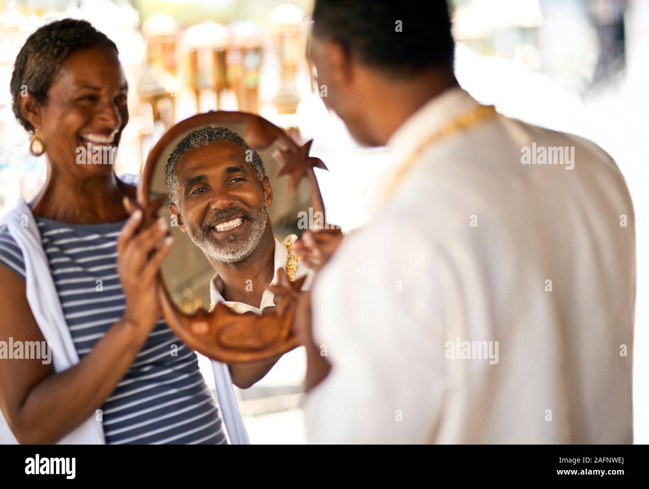 Mature man looking at his reflection while his wife holds up Mature man looking at his reflection while his wife holds up