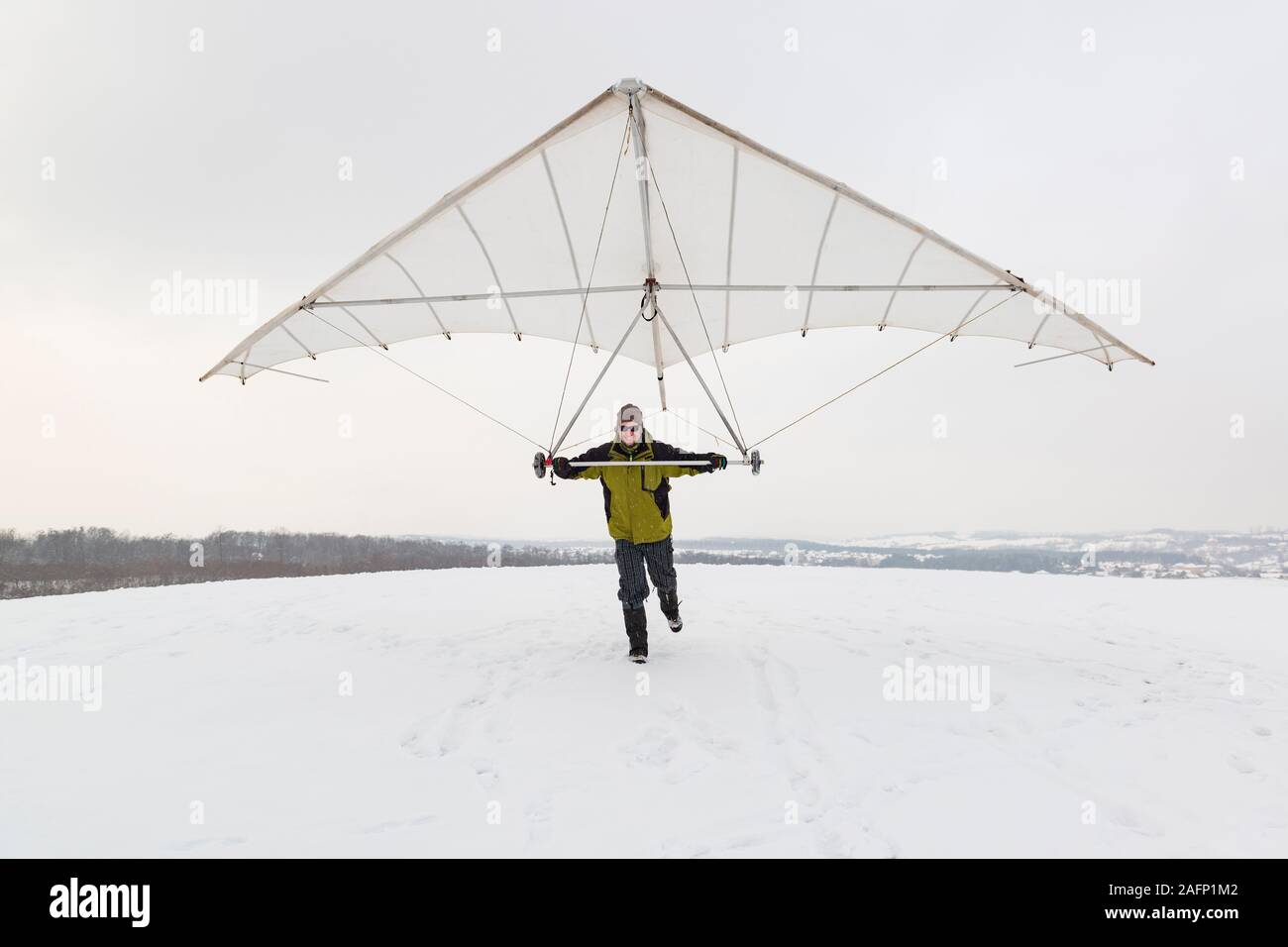 Happy man holds vintage hang glider wing. Hang gliding in winter. Stock Photo