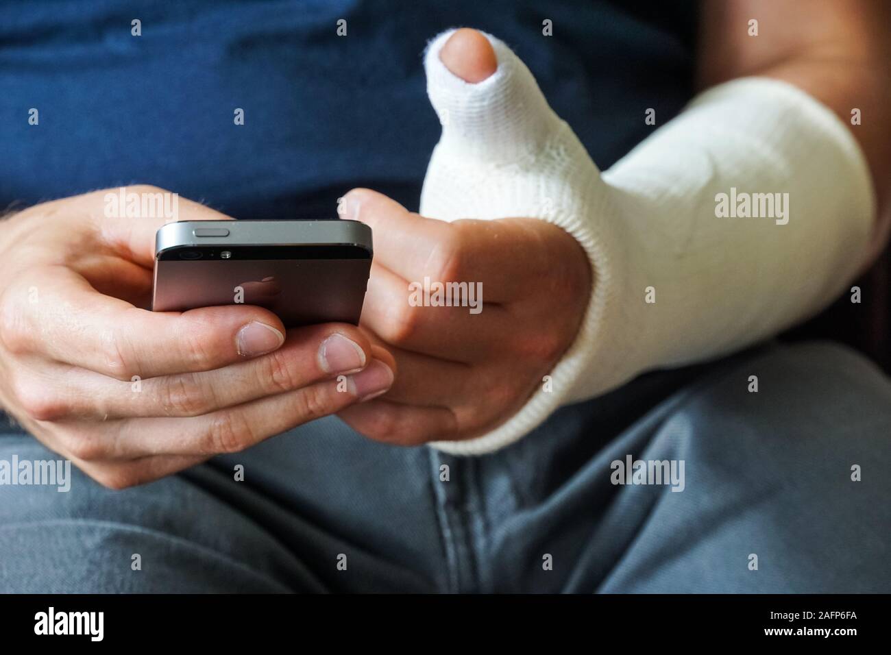 Man with plaster cast on broken hand, broken thumb,broken wrist using smartphone Stock Photo