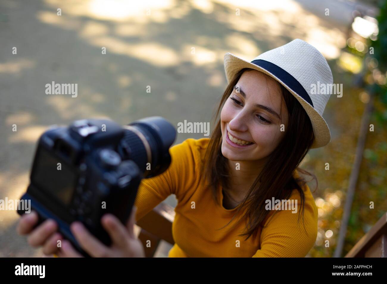 Woman vlogger and videographer with hat and dressed in yellow recording a video with a reflex camera for her travel blog. Concept of social networks a Stock Photo
