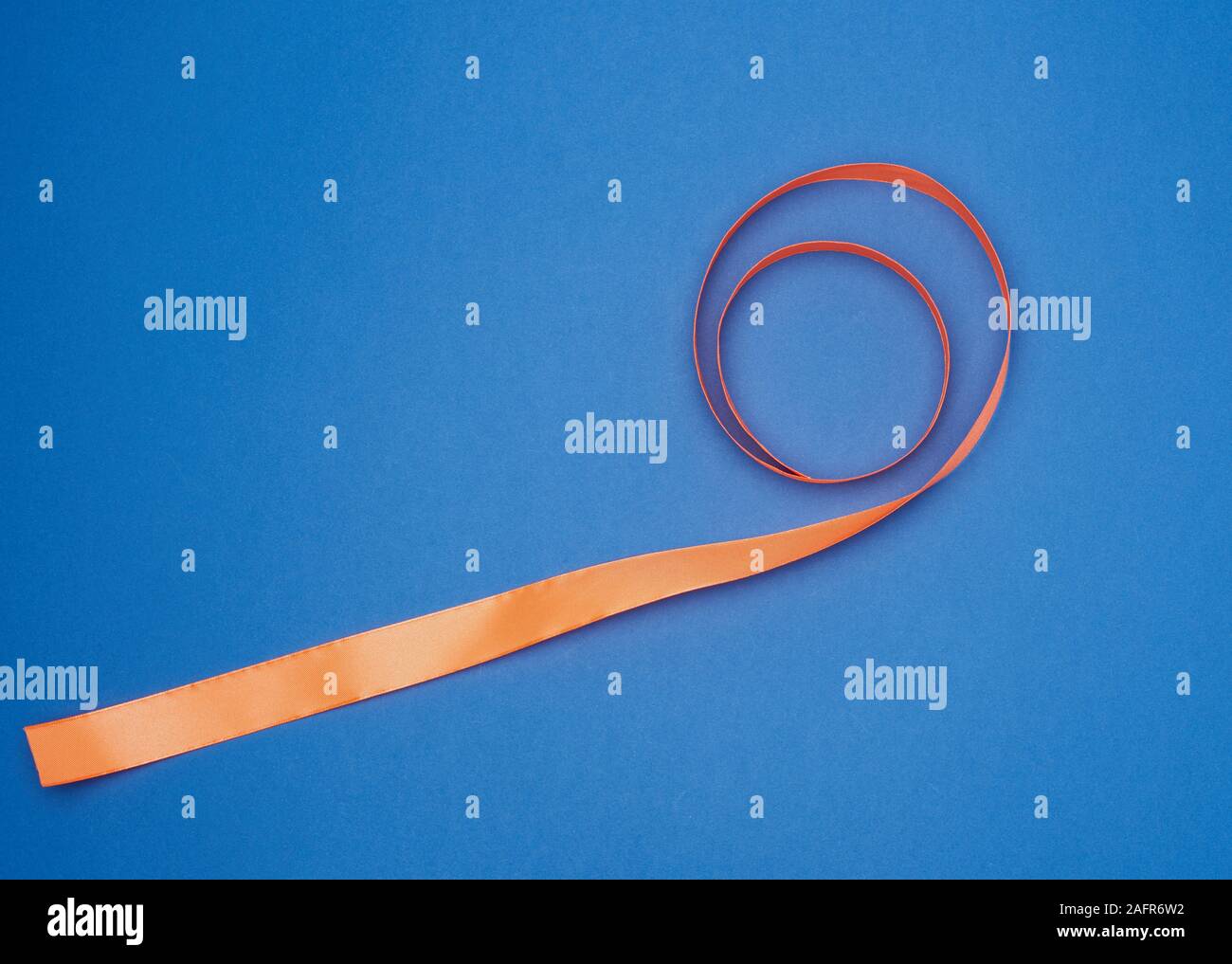 orange silk thin ribbon twisted on a blue background, trendy blue color ...