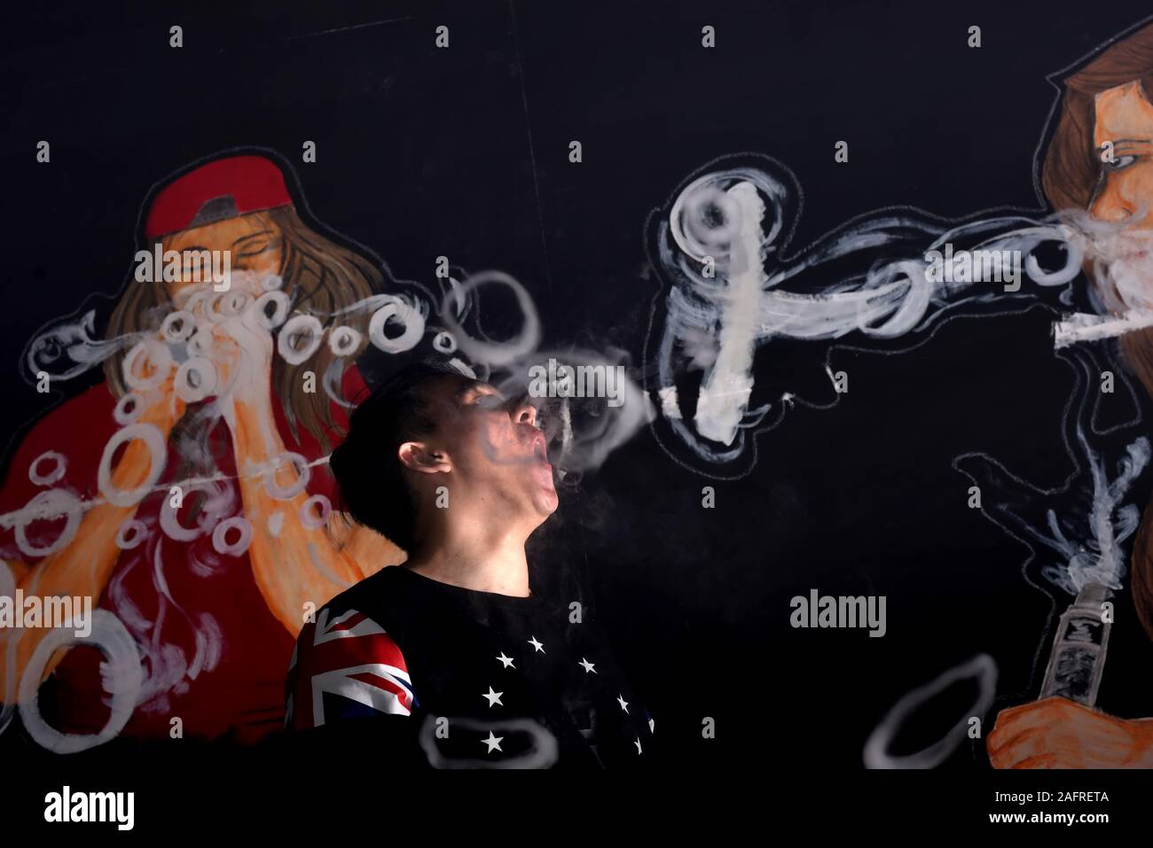 Osel Chandra, 21, demonstrates some of his vape cloud tricks in front of a vape shop's indoor murals. Stock Photo