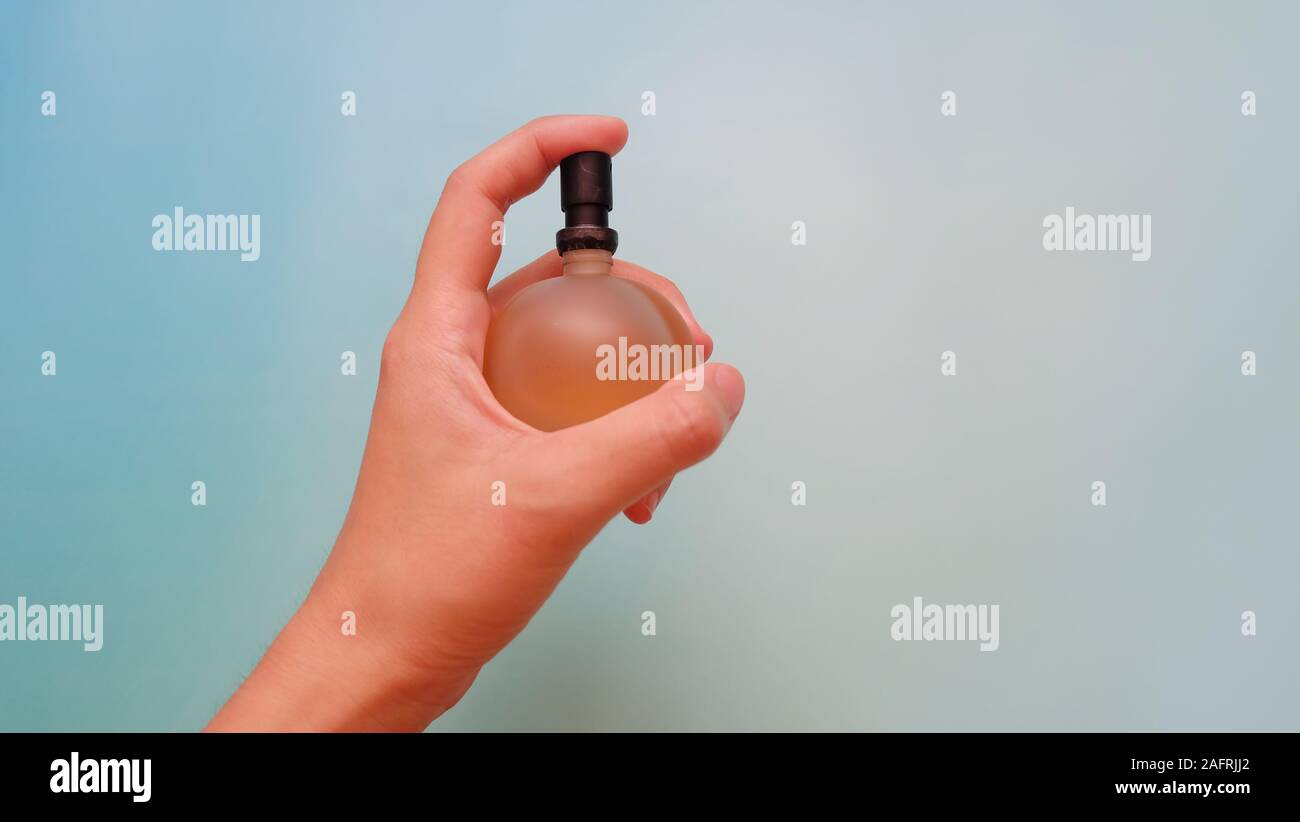 Hand holding a perfume spray bottle, with the finger pressing on the