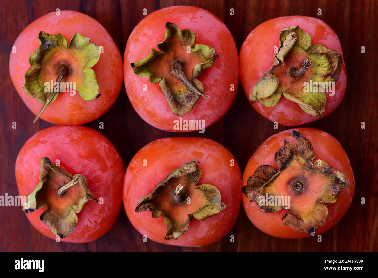 6 overripe orange persimmon fruits lie next to each other on dark wood Stock Photo