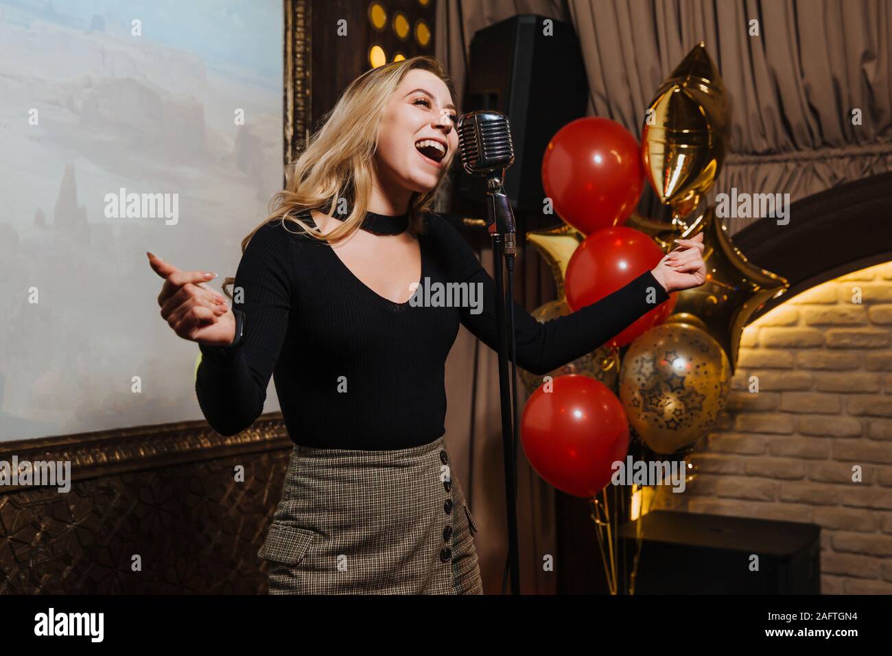 A beautiful young girl very energetically performs a beautiful karaoke song in a nightclub. Stock Photo