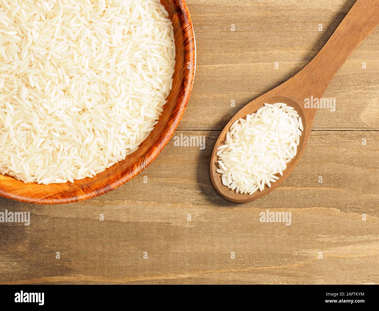 Rice in bowl and spoon on brown wooden background. Indian cuisine, ayurveda, naturopathy, modern apothecary concept Stock Photo