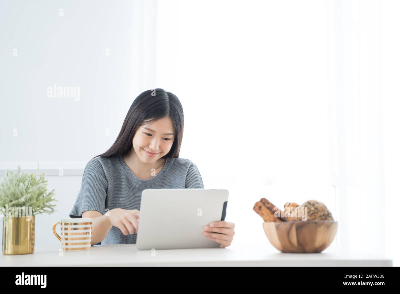 Young Asian woman using tablet at home and having breakfast in the morning .She reading on tablet. Stock Photo
