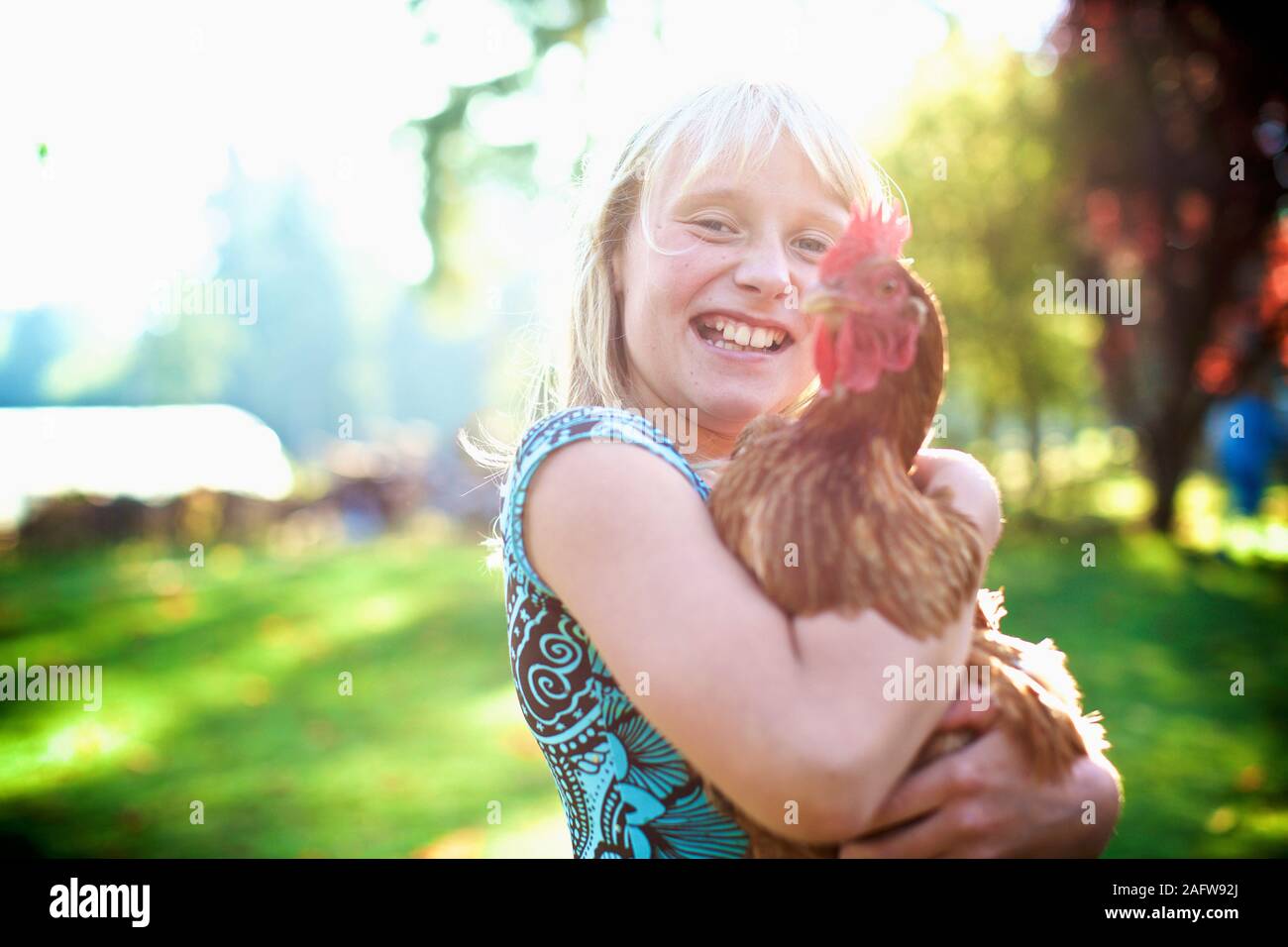 Portrait happy girl holding hen in sunny yard Stock Photo
