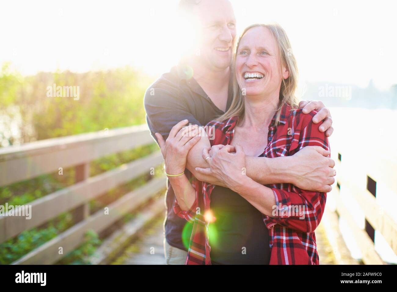 Portrait happy, affectionate couple hugging on sunny summer footbridge Stock Photo