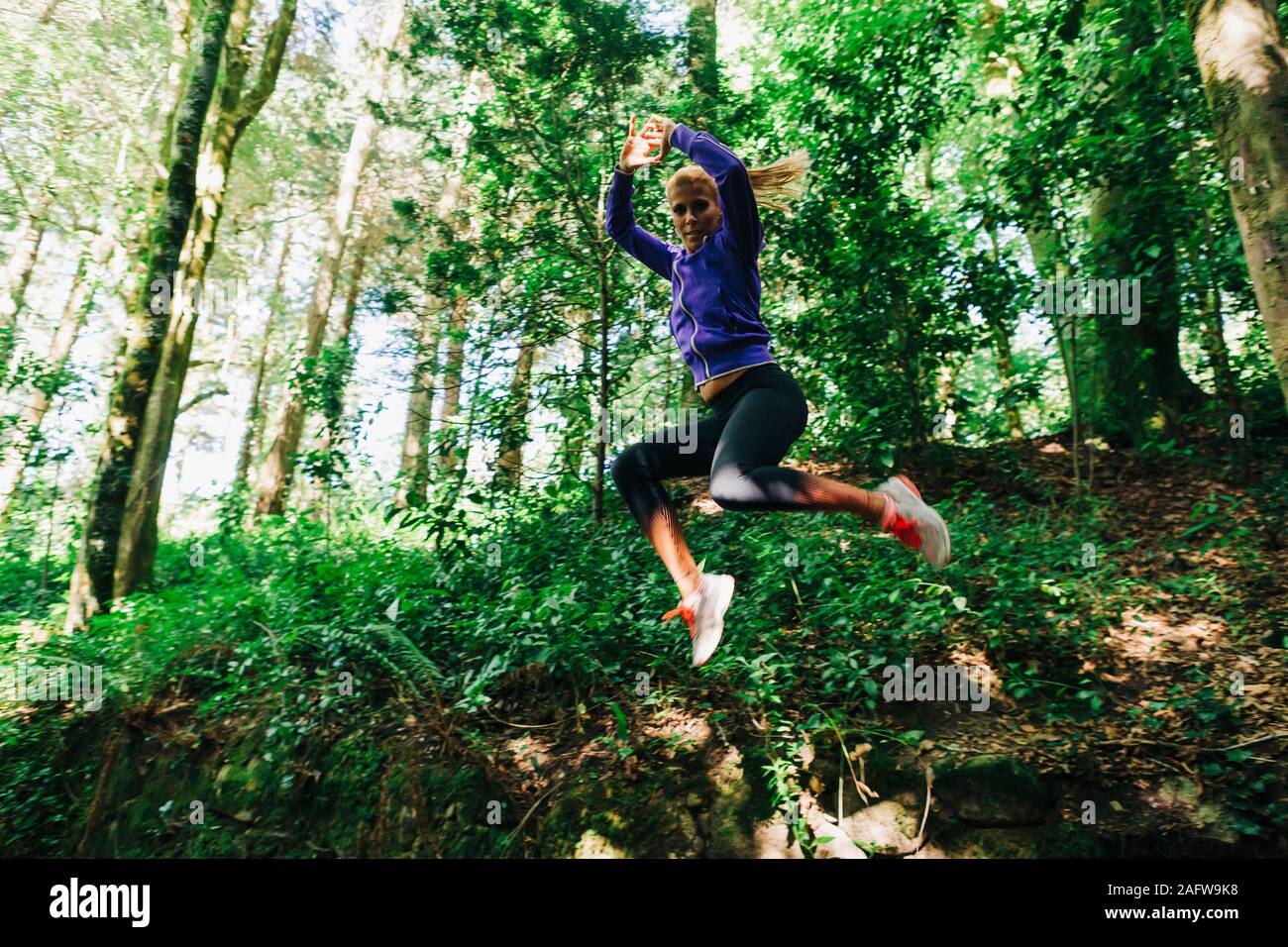 Portrait carefree female personal trainer hiking, jumping in forest Stock Photo