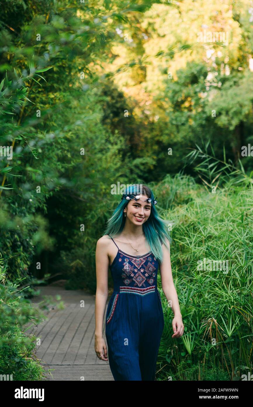 Portrait smiling, happy young woman with blue hair walking along footpath in lush park Stock Photo