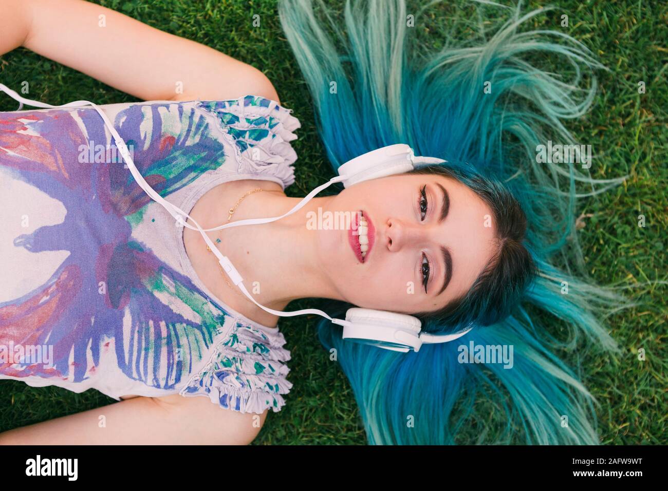 Overhead portrait young woman with blue hair listening to music with ...