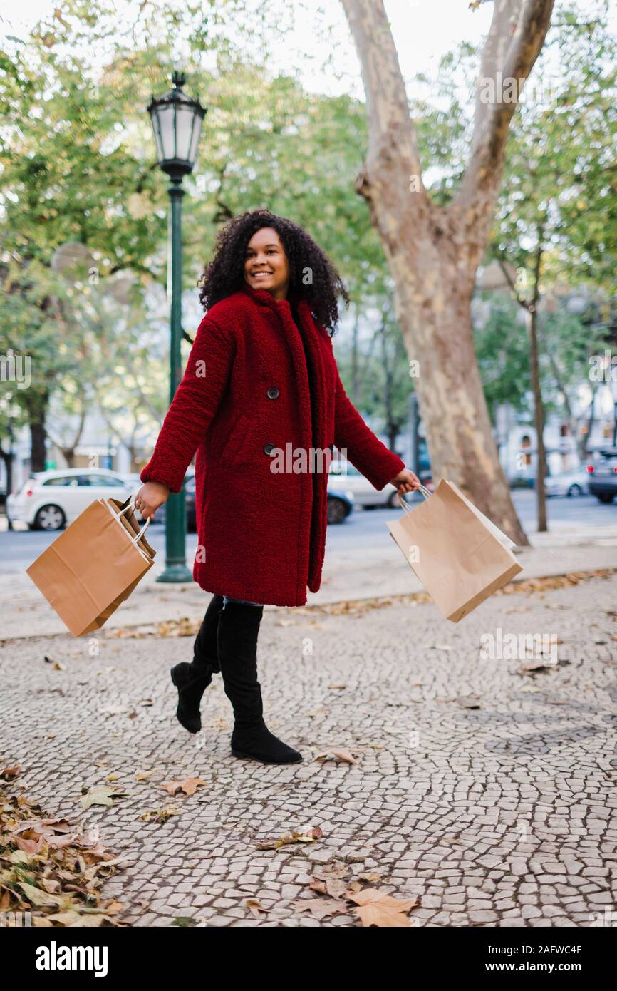 Portrait carefree young woman walking with shopping bags in urban autumn park Stock Photo