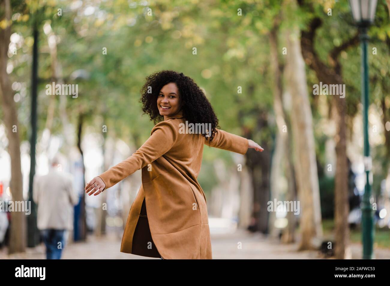 Portrait carefree young woman dancing on treelined sidewalk Stock Photo