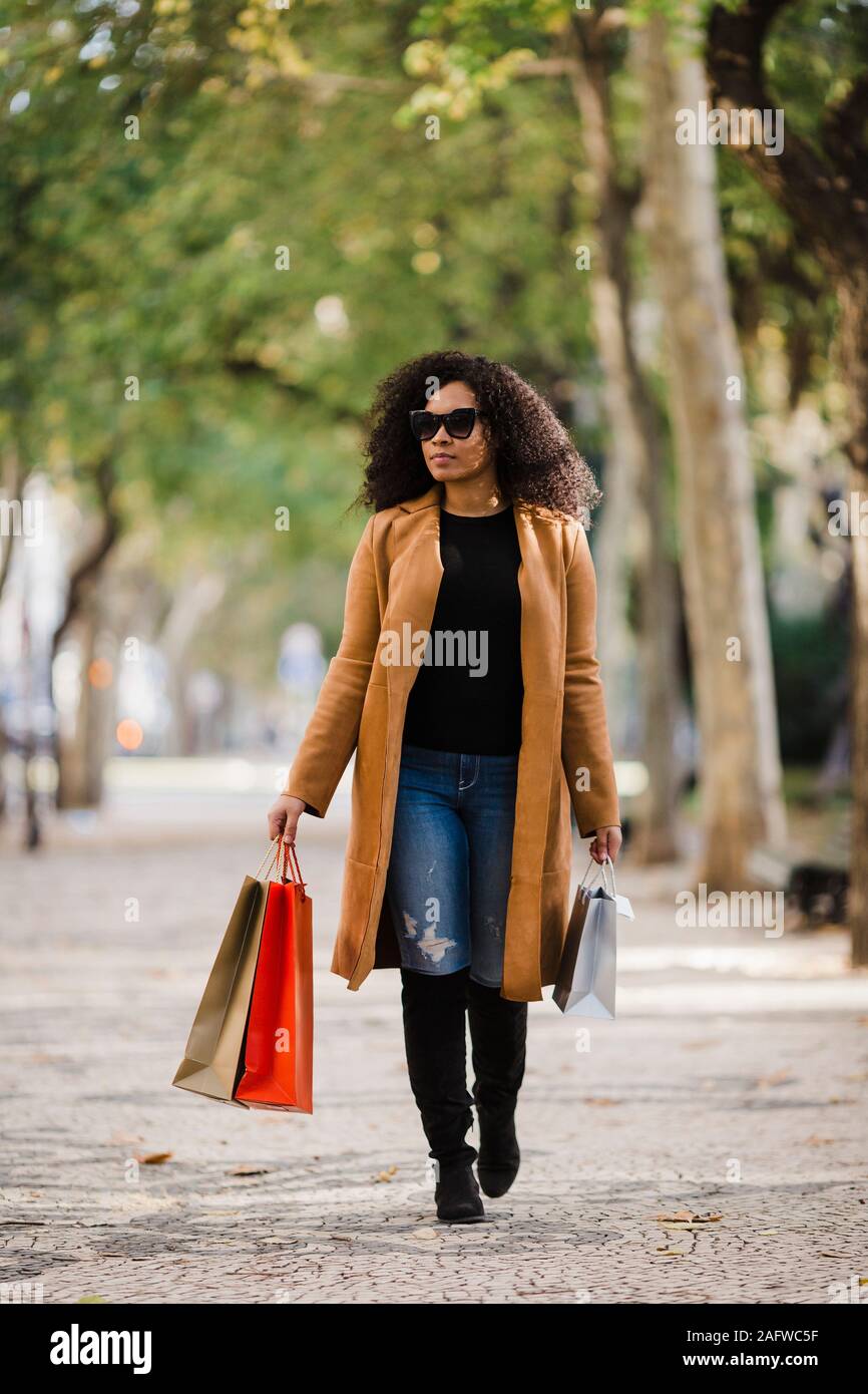 Stylish young woman walking with shopping bags on sidewalk Stock Photo