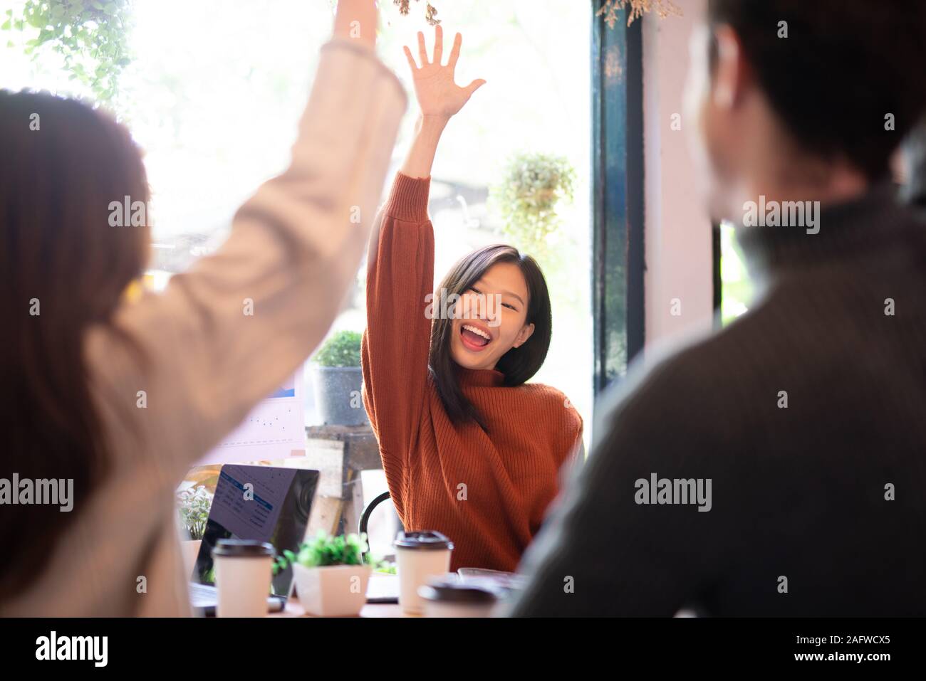 Asian woman and her team hand raised for happy winning success in coffee shop with team Stock Photo