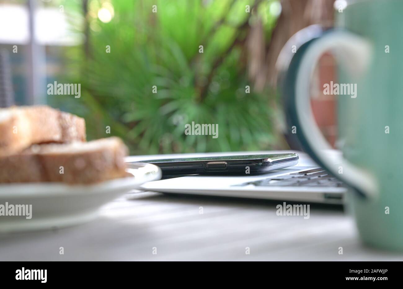 Working on the computer and cell phone while having breakfast. Work from home or flexi time concept. Stock Photo