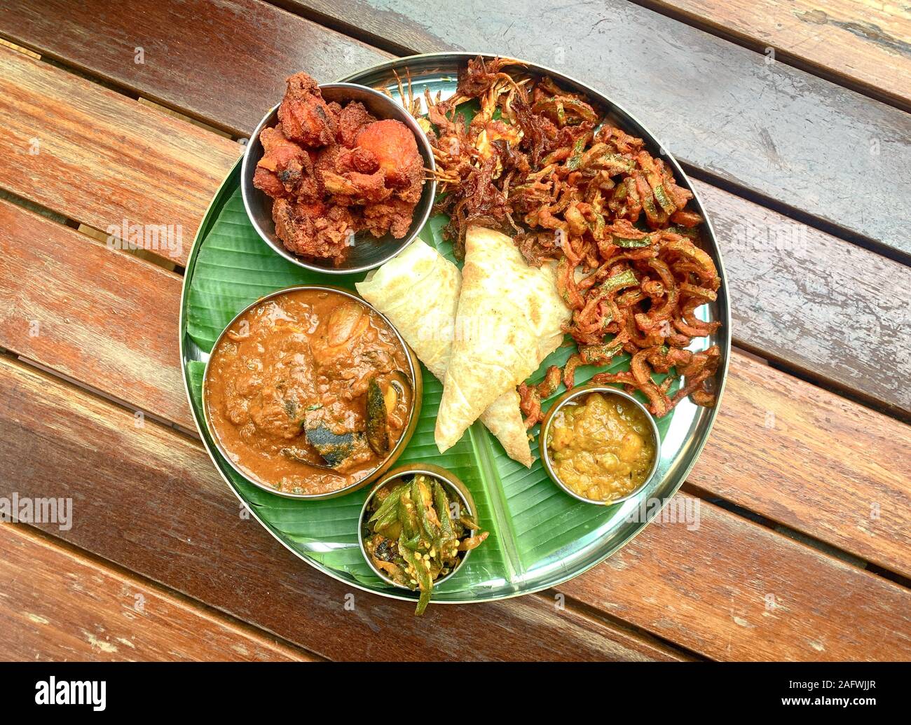 Delicious banana leaf dish, consists of fried chicken, curry seafood, lady fingers, potatoes and canai Stock Photo