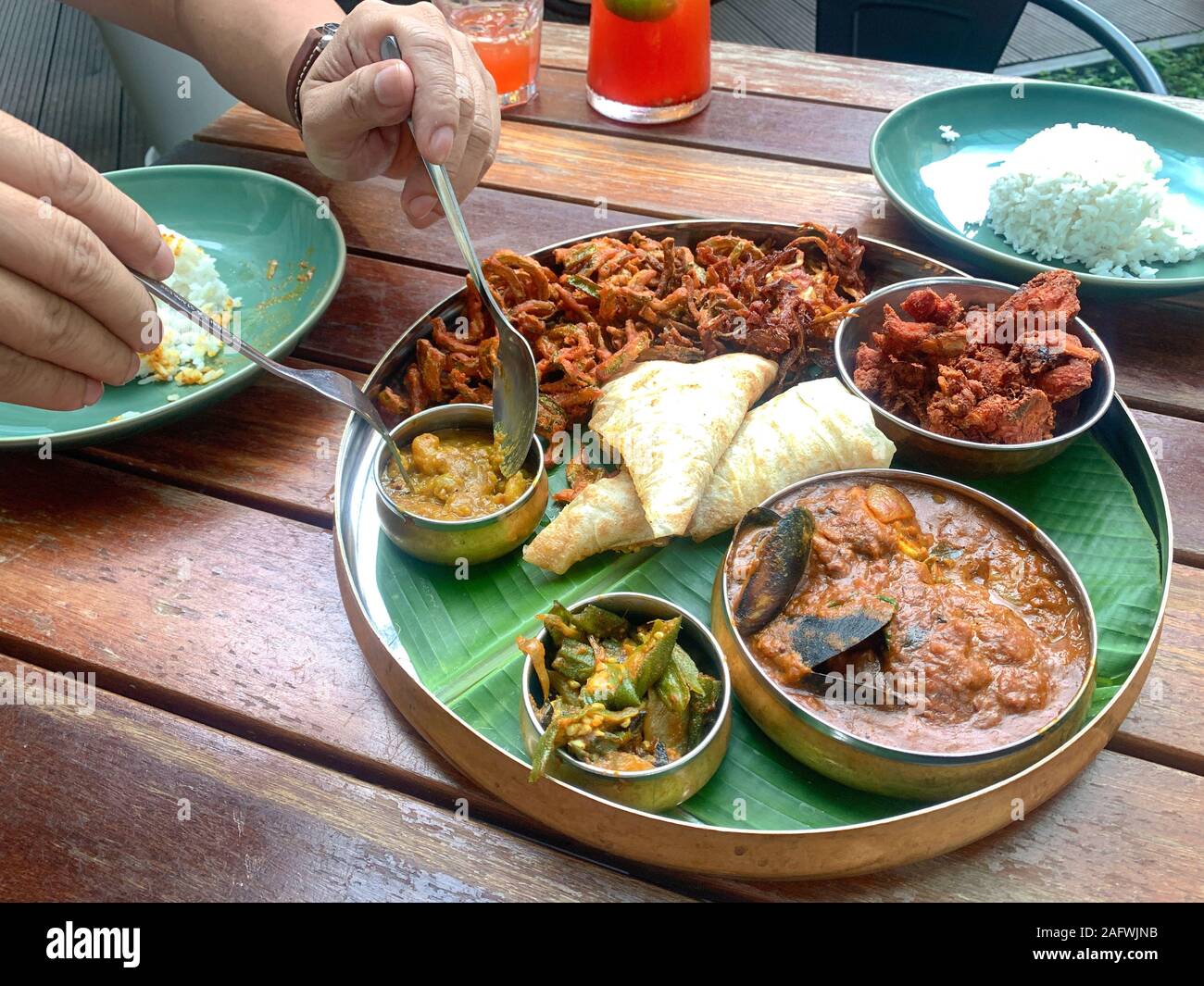 Man using fork and spoon to eat banana leaf dish, consists of fried chicken, curry seafood, lady fingerspotatoes and canai Stock Photo